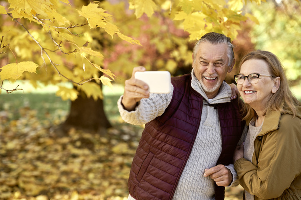 Senior woman and man making selfie at the park in autumn  - Fotoğraf, Görsel