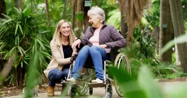 Старшая мать в инвалидной коляске сближается с дочерью, наслаждается семейным времяпрепровождением и весело проводит время в природном парке или общественном саду. Улыбающаяся, счастливая или заботливая женщина, говорящая и толкающая пожилую женщину на помощь в передвижении. - Кадры, видео