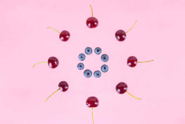 Berries of cherries and blueberries arranged in a circle. Pink background. Concept of berries season and proper nutrition. Flat lay. Copy space. - Fotoğraf, Görsel