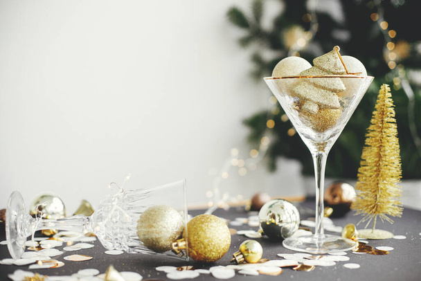 Stylish christmas glitter baubles in champagne glass and golden decorations on festive background. New year party creative concept. Merry Christmas and Happy New Year! Moody holiday banner - Foto, imagen