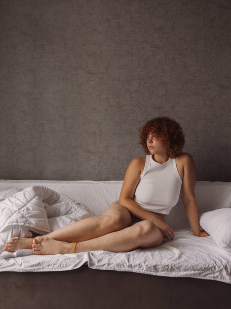 Beautiful girl with curly red hair on the bed in the morning  - Фото, изображение