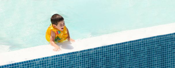 Красивый мальчик 5 лет в желтом плавательном жилете веселится в бассейне, баннер с местом для текста. - Фото, изображение