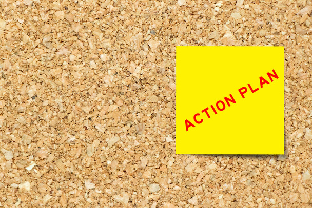 Yellow note paper with word action plan on cork board background with copy space - 写真・画像