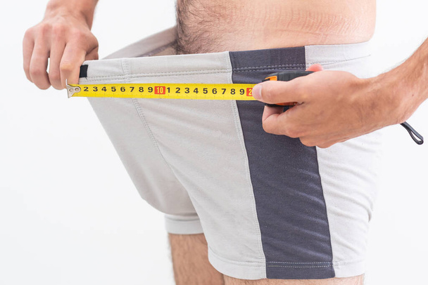 A man questioningly holds a measuring tape to his underpants - Photo, Image