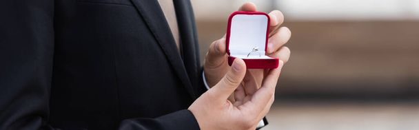 Cropped view of man in jacket holding box with engagement ring outdoors, banner  - Foto, Bild