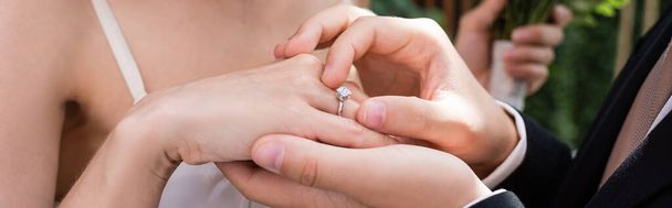 Cropped view of groom wearing ring on finger of bride outdoors, banner  - Photo, image