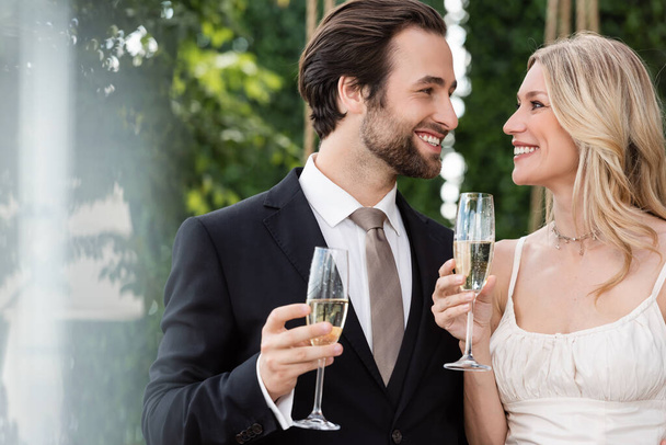 Cheerful newlyweds holding glasses of champagne outdoors  - Zdjęcie, obraz