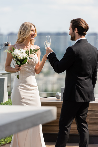 Cheerful newlyweds clinking with champagne on terrace of restaurant  - Фото, зображення