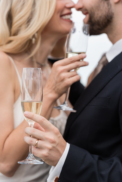 Cropped view of champagne in hand of groom kissing bride outdoors  - Fotografie, Obrázek