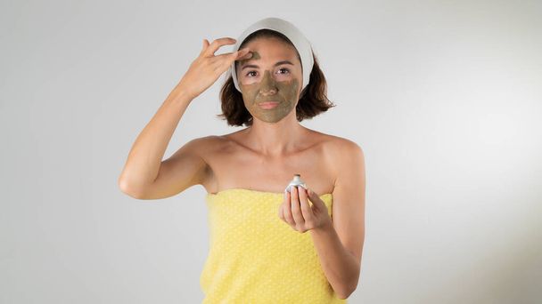 Uma mulher em uma toalha depois de um chuveiro aplica uma máscara de barro em seu rosto autocuidado em casa. Foto de alta qualidade - Foto, Imagem