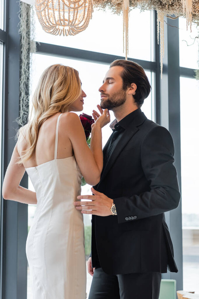 Blonde woman holding flowers and touching man in suit in restaurant  - Foto, Imagem