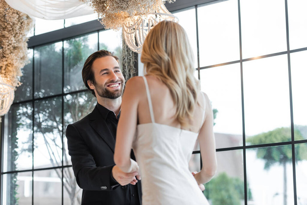 Smiling man in suit holding hands of blurred girlfriend in restaurant  - Foto, imagen