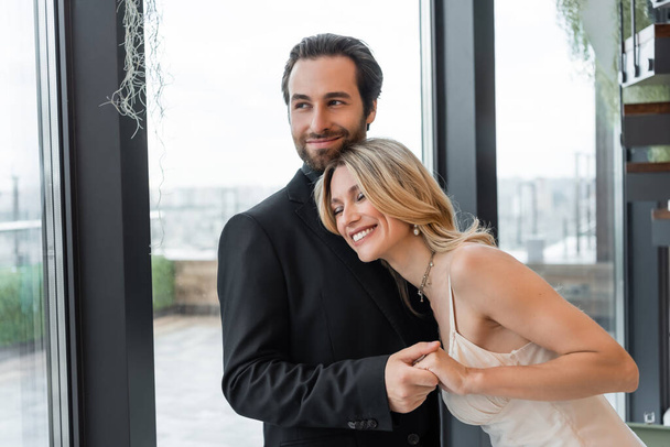 Smiling man in suit holding hand of happy girlfriend in dress in restaurant  - Fotó, kép