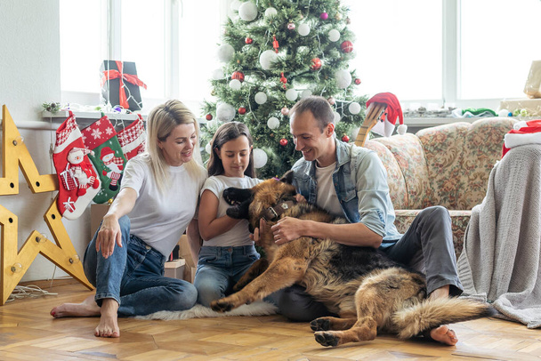 happy family and cute dog having fun at christmas tree. atmospheric emotional moments. merry christmas and happy new year concept - Fotó, kép