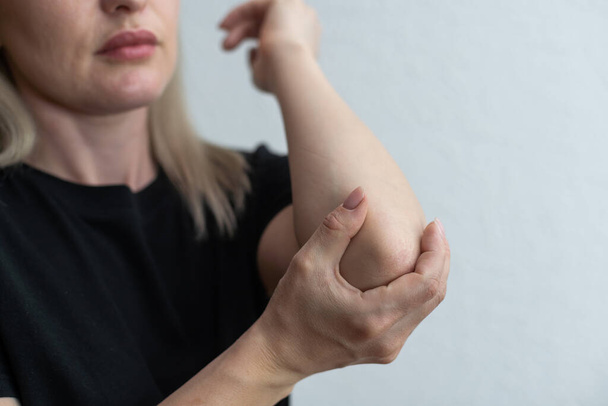 Женщины страдают от боли в локте, держась за руку, чтобы заметить боль в локте. Концепция боли в руках и травм. - Фото, изображение