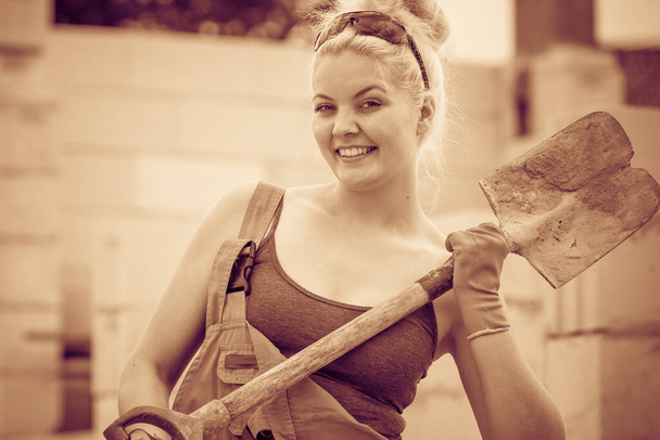 Woman worker using shovel standing on industrial construction site, working hard on house renovation. - Fotografie, Obrázek