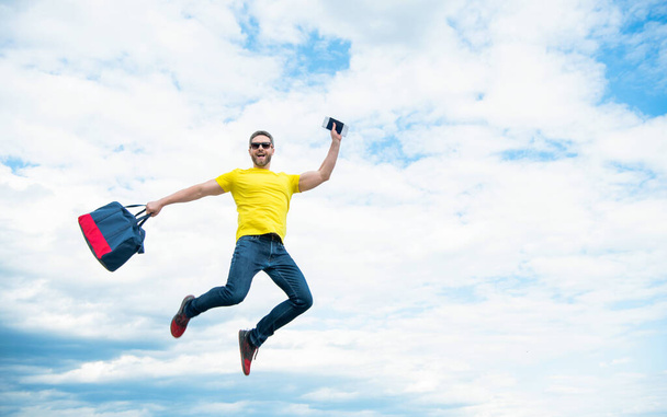 Active guy jumping with travel bag midair sky background, copy space. - Photo, Image