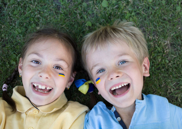 faces of two laughing happy children, boy and girl of 6-7 years old in yellow and blue t-shirts, lie on the grass. view from above. independence Day. Children of Ukraine for Peace. Support Ukraine - Photo, image