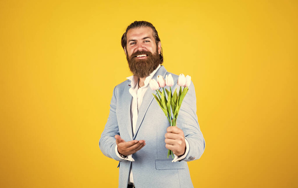 紳士は花束を持ってる。フラワーショップのコンセプト。髭と髪型の男。祝日とお祝い。母親や女性の日のための花の贈り物。チューリップの花を持つ幸せな男. - 写真・画像