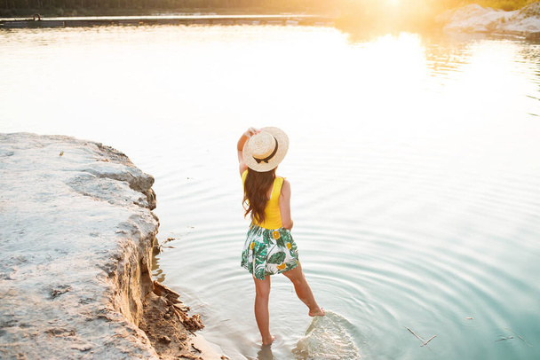 Чудова молода дівчина позує на тлі заходу сонця, стоячи у воді, насолоджуючись літньою подорожжю до озера
. - Фото, зображення