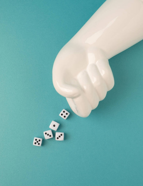 Artificial hand throwing dice on a teal background. Gambling, risk conceptual flat lay. - Фото, изображение