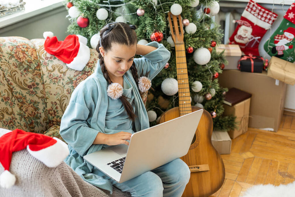 χειμερινές διακοπές, την τεχνολογία και τα παιδιά έννοια - μικρό κορίτσι φοιτητής με φορητό υπολογιστή στο σπίτι πάνω από το χριστουγεννιάτικο δέντρο φόντο - Φωτογραφία, εικόνα