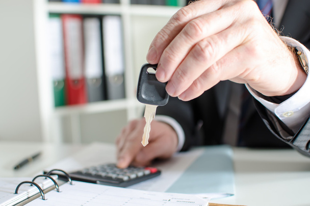 Car salesman holding a key and calculating a price - Фото, изображение