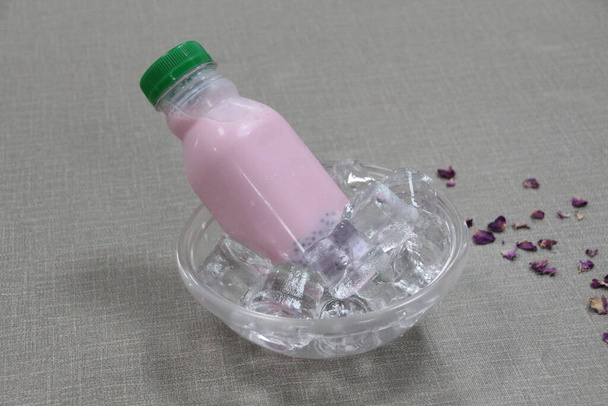 Eine Flasche Milch mit Rosensirup und Basilikumkernen serviert in Eiswürfelschale Seitenansicht auf grauem Hintergrund - Foto, Bild