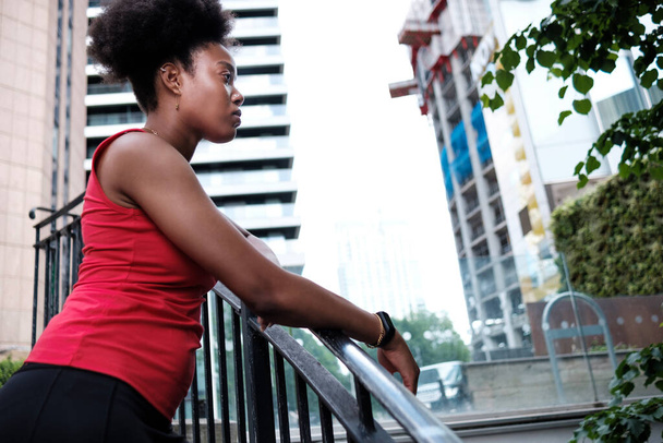 A fit young black woman is posing on stairs and and looking away. Motivation and determination concept. - 写真・画像