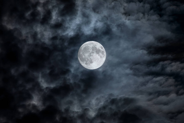 Full moon at night. The illuminated face of the moon is wrapped in a cloud cover that covers it in a veiled way. - Foto, Imagen