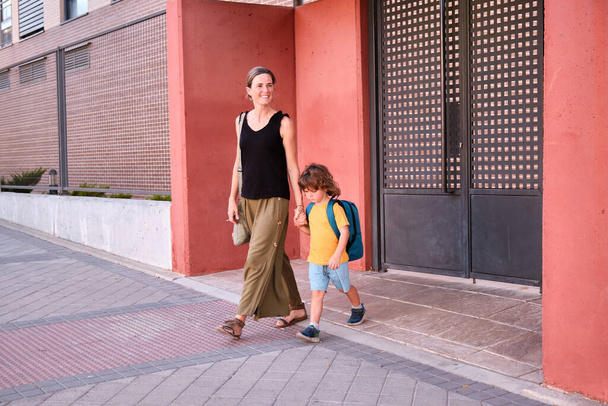 Parent and pupil of preschool. Woman and boy with backpack behind back. Beginning of lessons. First day of fall. - Foto, imagen