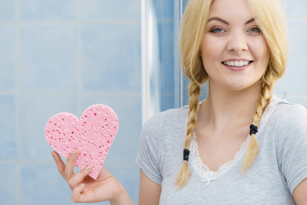 Young pretty adorable woman having two cute braids on blonde hair holding pink sponge in heart shape. Haircare and hairstyling concept. - Valokuva, kuva