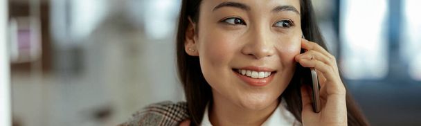 Primer plano de la sonriente mujer de negocios asiática haciendo llamada telefónica de pie en la oficina. Foto de alta calidad - Foto, Imagen