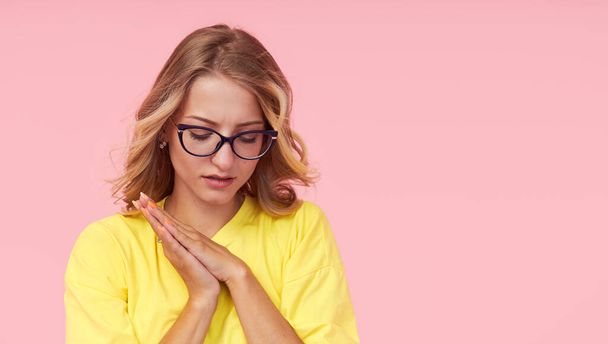 Portrait of young woman in eyeglasses, yellow t-shirt on a pink background. Surprised girl looks to the right with her eyes wide open. Wow face - Foto, immagini