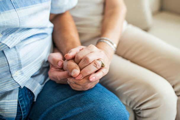 Close up of mature old husband and wife hold hands show love and care. Senior couple holding hands while sitting together at home. Elderly relationships, marriage concept - Photo, image