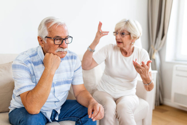 Senior couple having argument on the couch at home in the living room. Woman and man emotions gesturing with hands. Senior couple arguing - Foto, Imagen