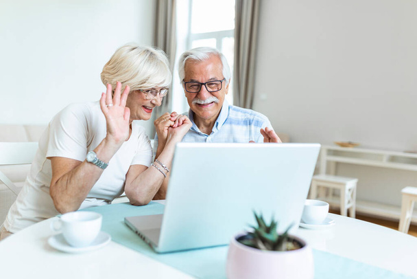 Ευτυχισμένο ζευγάρι της οικογένειας μιλάμε με τους φίλους και την οικογένεια χρησιμοποιώντας φορητό υπολογιστή, έκπληκτος ηλικιωμένη γυναίκα κοιτάζοντας τον υπολογιστή χαιρετώντας και χαμογελώντας. - Φωτογραφία, εικόνα