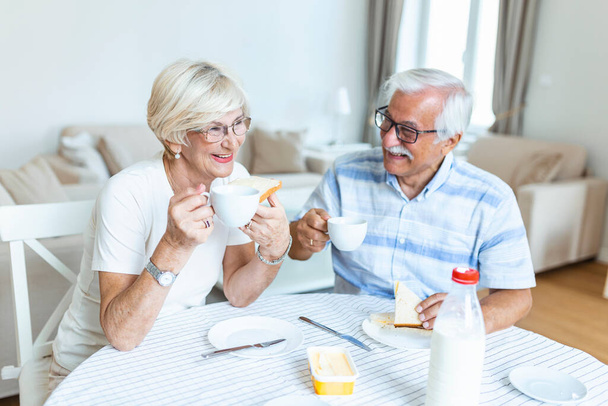 Το ηλικιωμένο ζευγάρι φτιάχνει σάντουιτς για πρωινό. Ευτυχισμένο ηλικιωμένο ζευγάρι που επικοινωνεί απολαμβάνοντας το πρωινό του. Ηλικιωμένο ζευγάρι διασκεδάζει. - Φωτογραφία, εικόνα
