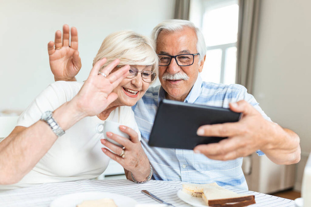 Το ηλικιωμένο ζευγάρι μιλάει στο διαδίκτυο μέσω σύνδεσης βίντεο στο tablet. Έχοντας ωραίο χρόνο με τους φίλους και την οικογένεια μέσω video call.Holding τα χέρια τους μαζί - Φωτογραφία, εικόνα
