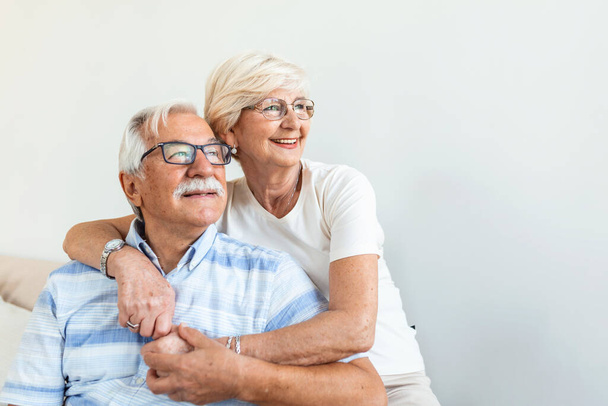 Portrait loving older wife hugging husband sitting on cozy couch. Happy senior mature couple smilling and looking at camera, posing for family photo at home. Elderly couple feeling happy - Photo, image