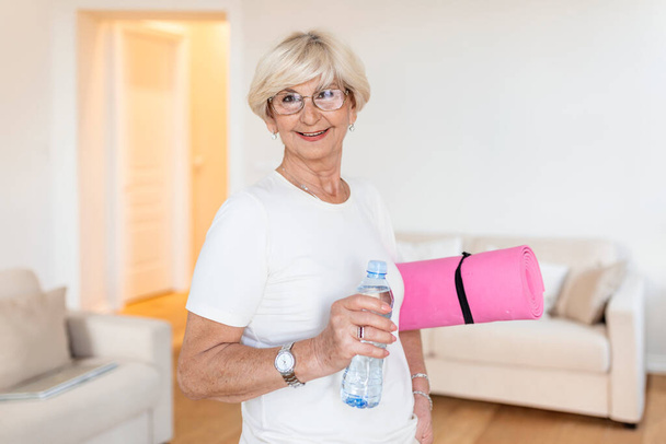Mature Woman getting ready for a workout. Elderly woman ready for working out. Refreshment after training. Sporty old woman drinking water - Zdjęcie, obraz