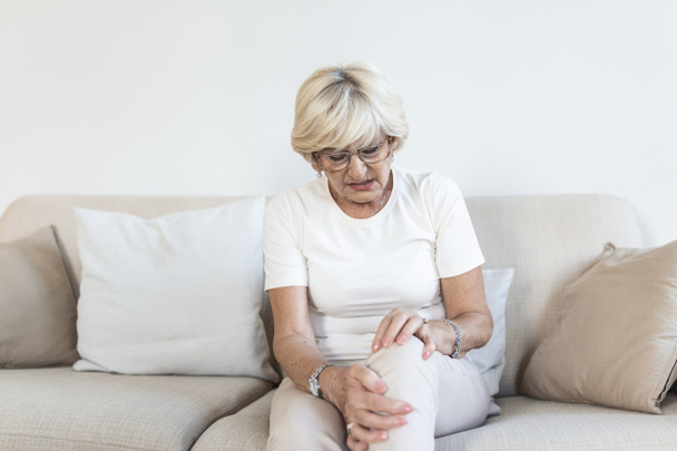 Senior woman holding the knee with pain. Old age, health problem and people concept - senior woman suffering from pain in leg at home. Elderly woman suffering from pain in knee at home - Zdjęcie, obraz