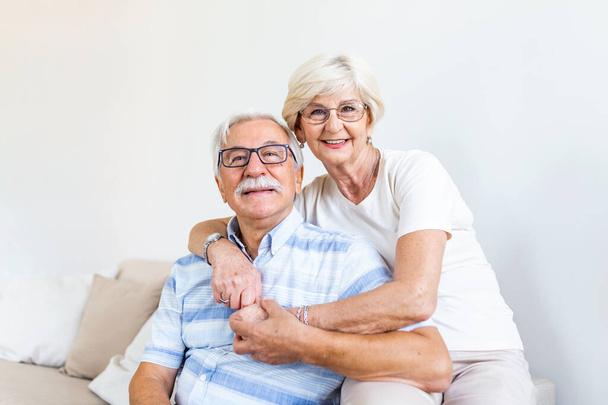 Portrait loving older wife hugging husband sitting on cozy couch. Happy senior mature couple smilling and looking at camera, posing for family photo at home. Elderly couple feeling happy - Fotó, kép
