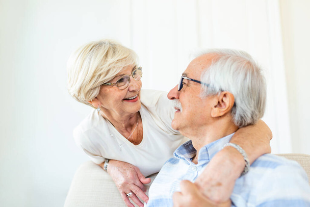 Πορτρέτο του ευτυχισμένου ηλικιωμένου ζευγαριού αγκαλιάζονται στο σαλόνι στο σπίτι. Ηλικιωμένα ζευγάρια κοιτάζονται με αγάπη και χαμόγελο - Φωτογραφία, εικόνα