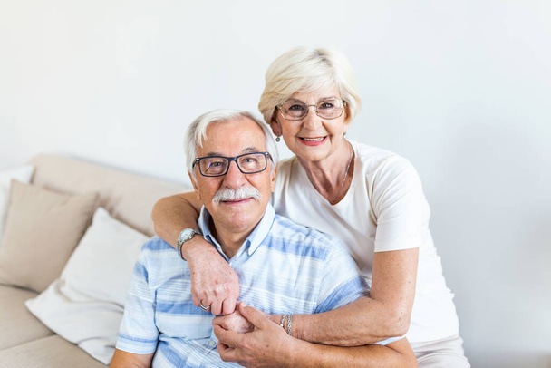 Portrait loving older wife hugging husband sitting on cozy couch. Happy senior mature couple smilling and looking at camera, posing for family photo at home. Elderly couple feeling happy - Foto, afbeelding