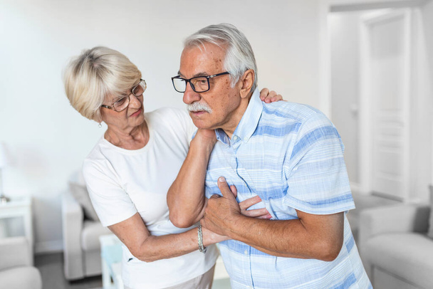 Senior man with neck pain and concerned elderly woman at home - Foto, afbeelding