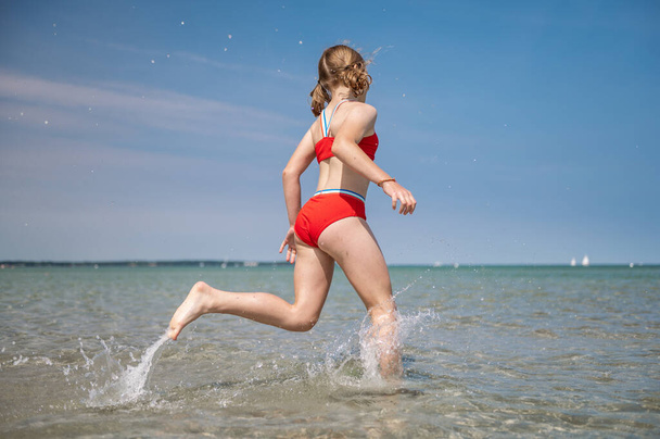 Happy teen child girl running and splashing water in turquoise sea at summer holidays - Φωτογραφία, εικόνα