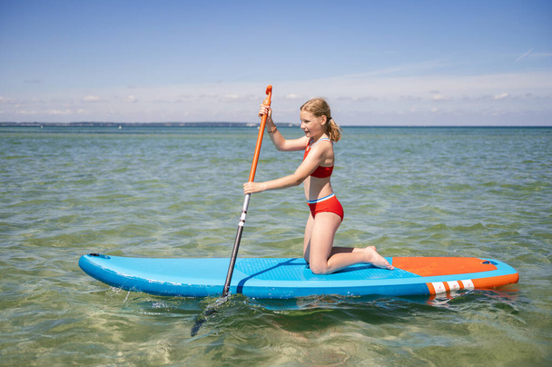 Beautiful child girl practice paddling on surfboard in sea at summer vocation - Fotoğraf, Görsel