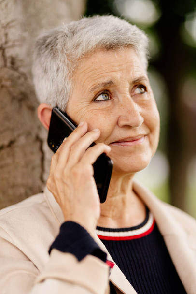 натуральний портрет літньої жінки з сірим волоссям, з безтурботним і щасливим використанням її мобільного телефону
. - Фото, зображення