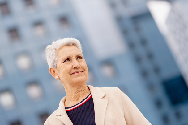 natural portrait of older woman with gray hair in the city, smiling and looking at infinity. - Foto, Bild
